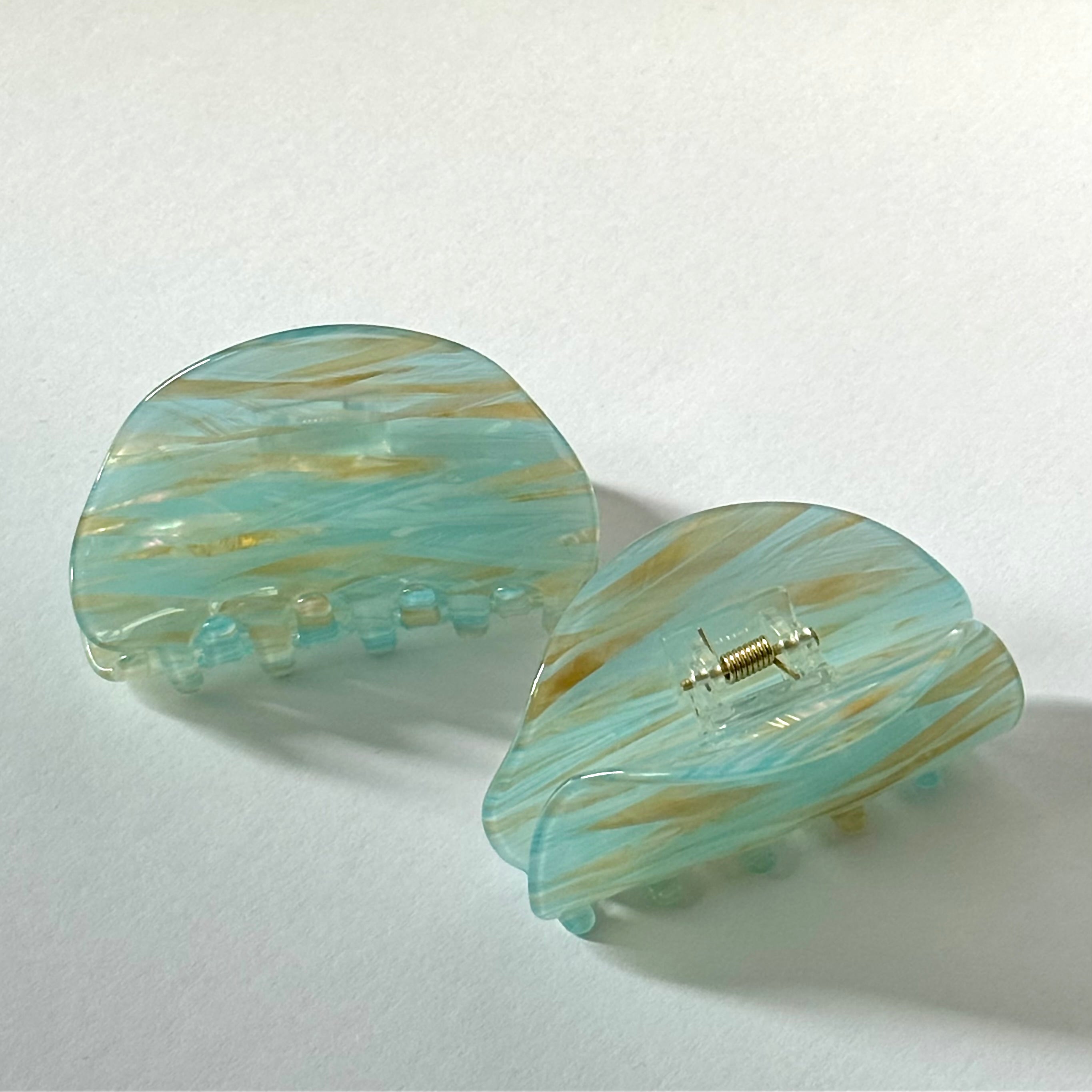 Pair of light blue and gold marbled hair clips on a white background